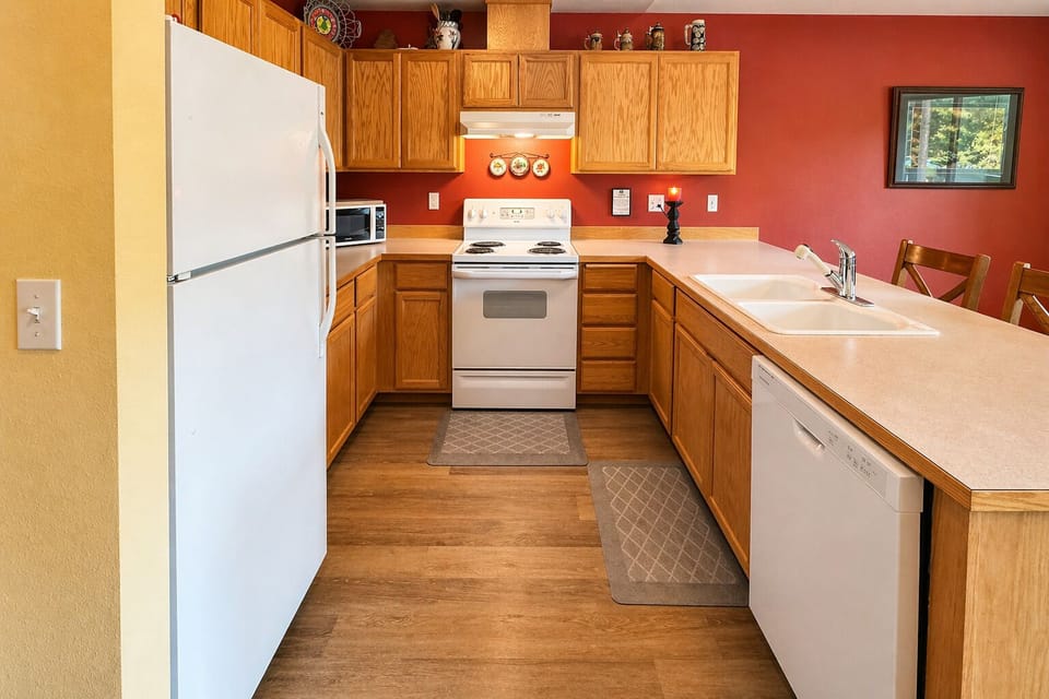 Your fully equipped kitchen features warm wood cabinets, white appliances, and rich red walls creating a welcoming space for cooking.