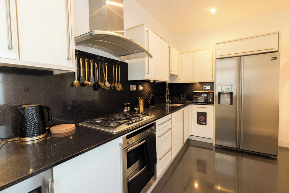 A sleek kitchen with granite counters, gold utensils and a wine cooler.
