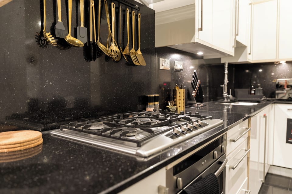A sleek kitchen with granite counters, gold utensils and a wine cooler.