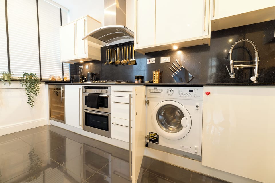 A sleek kitchen with granite counters, gold utensils and a wine cooler.