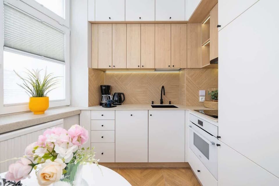 A modern kitchen with white and wooden cabinets, integrated appliances, and a minimalist design, offering a clean and practical cooking space.
