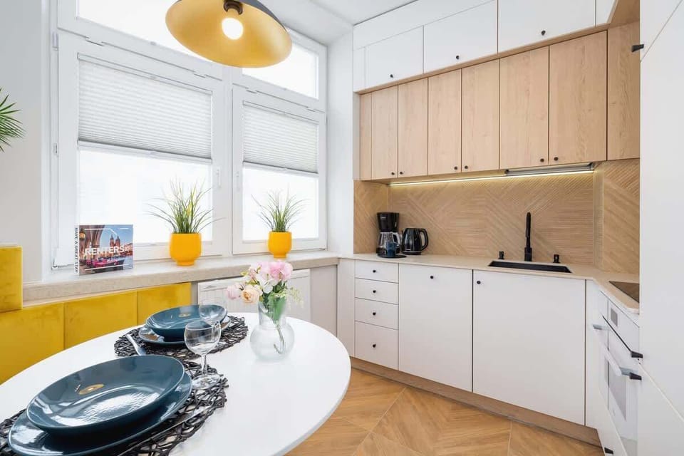 Another angle of the dining area showcasing a round table set with elegant blue plates, yellow accents, and large windows allowing plenty of natural light.
