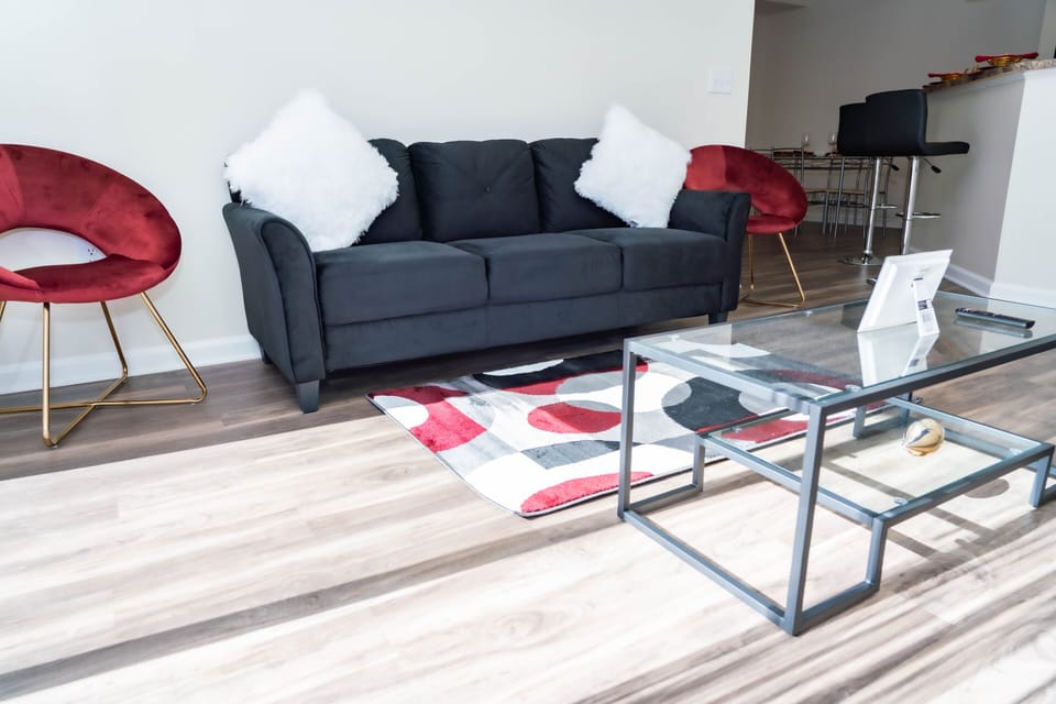 Black couch with white pillows and burgandy sitting chairs. 
Black glass table.