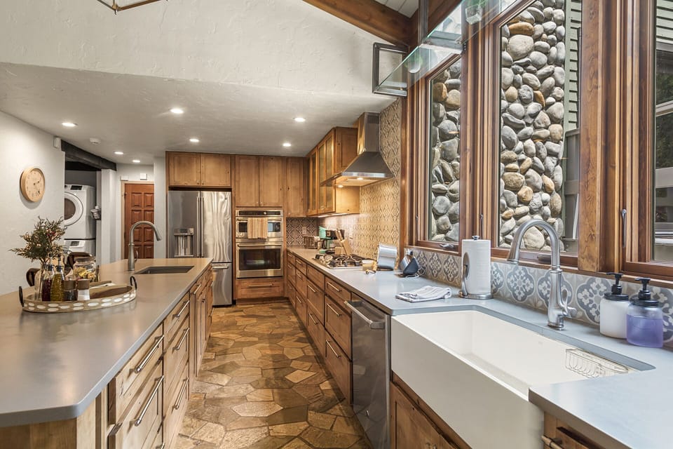 Gathering Island Kitchen — Stainless appliances, double sinks, and a generous island with seating—perfect for sipping wine, sharing stories, and watching the creek drift by. 🍷🏞️
