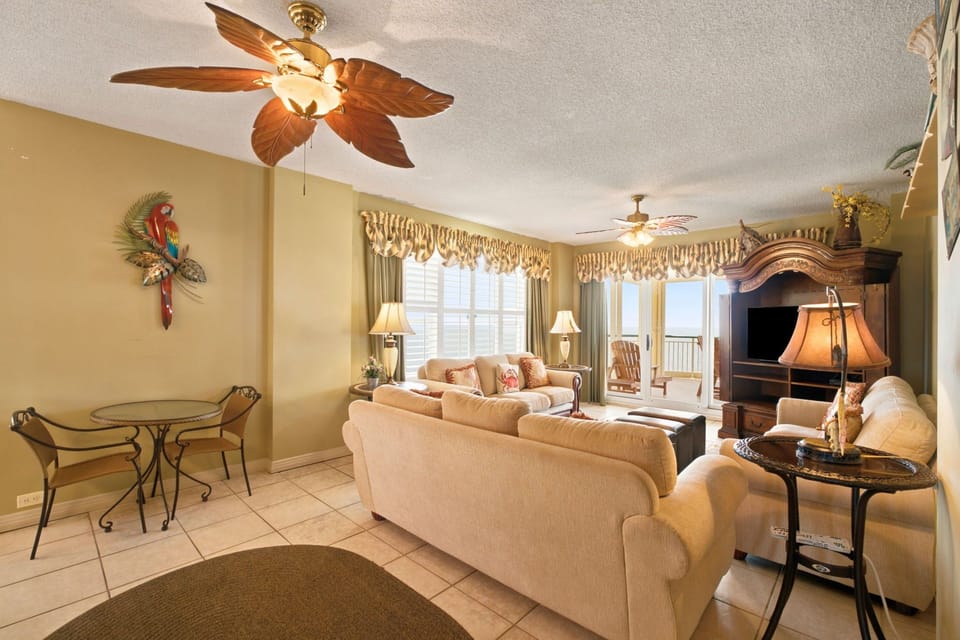 Beach Colony W13A- Relax in your comfortable living space with tropical-themed décor, ceiling fan, entertainment center, and access to your private balcony with views beyond.