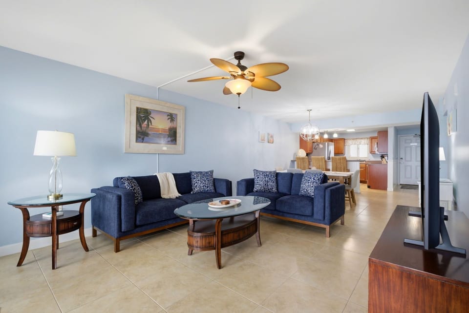 Sandy Key 637-  Step into your spacious living room with soothing coastal tones, plush navy seating, and ceiling fan above. The open layout flows seamlessly into the fully equipped kitchen, perfect for relaxing after exploring.