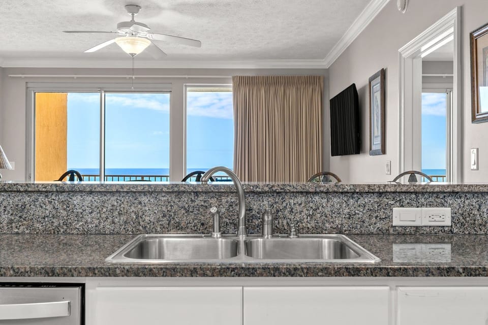 Modern kitchen sink area with granite countertops and ocean views through large windows.