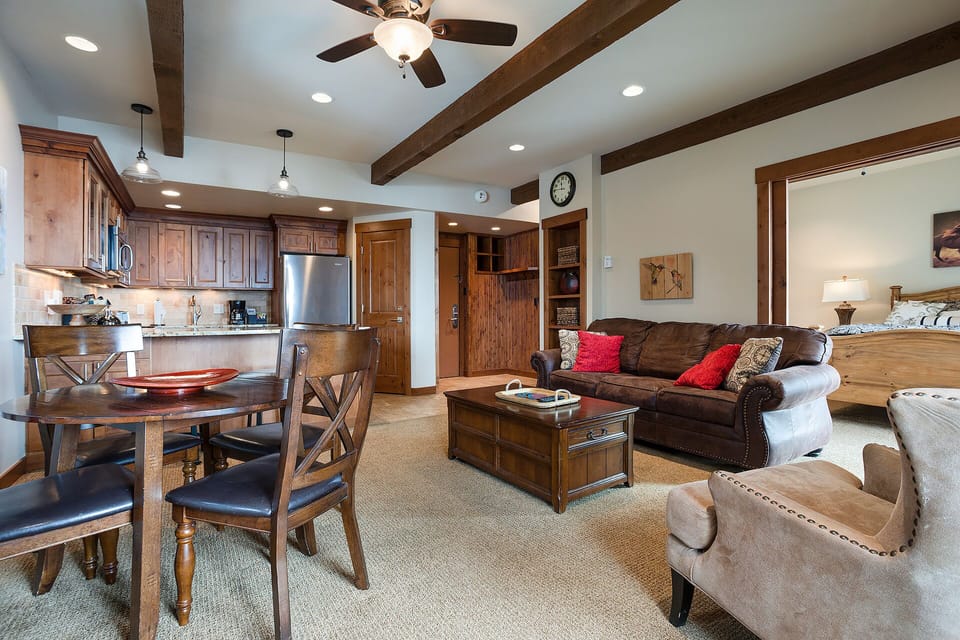 Relax in your spacious open-concept suite featuring exposed wood beams, a fully-equipped kitchen, and cozy living area with leather seating.