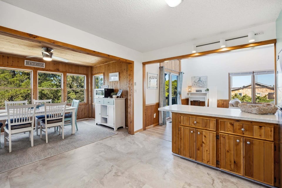 Just off the kitchen, the bright sunroom doubles as a dining area, featuring wood-paneled walls and large windows that fill the space with natural light—perfect for enjoying meals at sunset.
