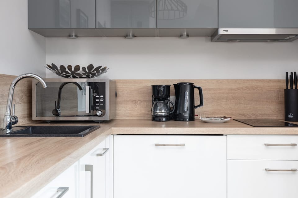 A modern, minimalist kitchen with white cabinetry, wood-textured countertops, and sleek appliances.
