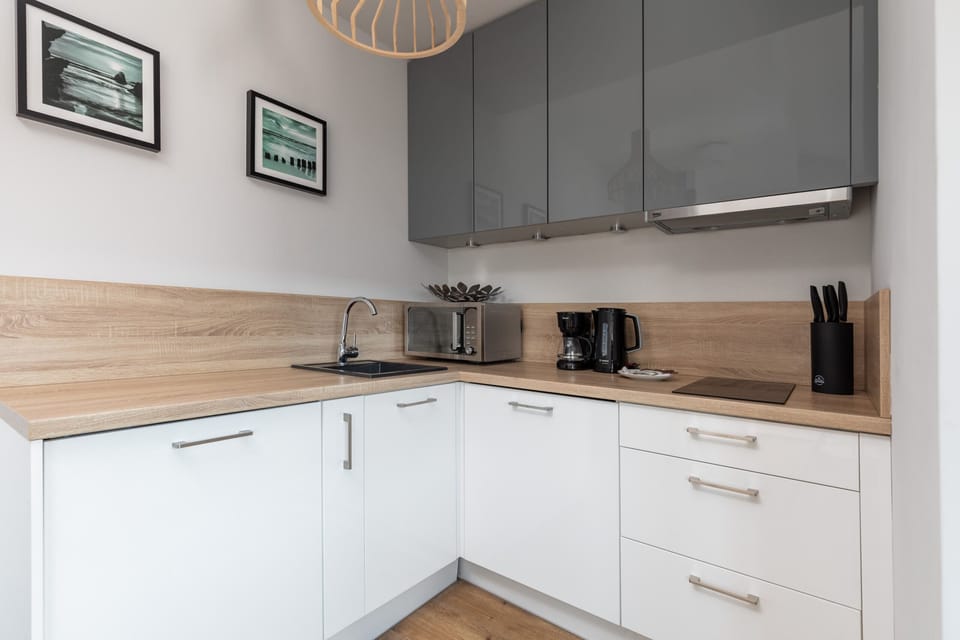 A modern, minimalist kitchen with white cabinetry, wood-textured countertops, and sleek appliances.