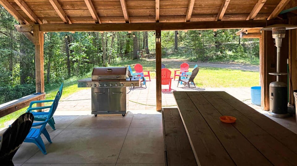 Covered outdoor patio with a grill and seating overlooking a wooded yard.