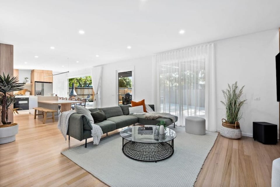This beautifully designed open-plan living space is filled with natural light, featuring a sleek comfortable couch, dining area, and direct access to a private outdoor entertaining area