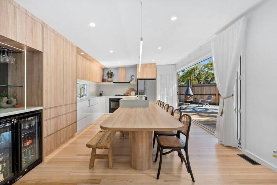 This stunning open-plan kitchen and dining space features sleek timber finishes, a wine fridge, and seamless indoor-outdoor flow to a sun-drenched courtyard with a chiminea