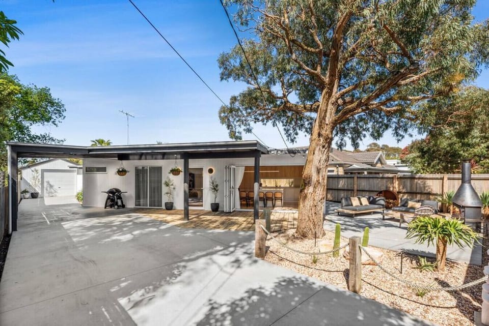 Relax in this stylish outdoor oasis featuring a spacious deck, lush landscaping, ample seating, and a wood-fired chiminea under the shade of a grand eucalyptus tree