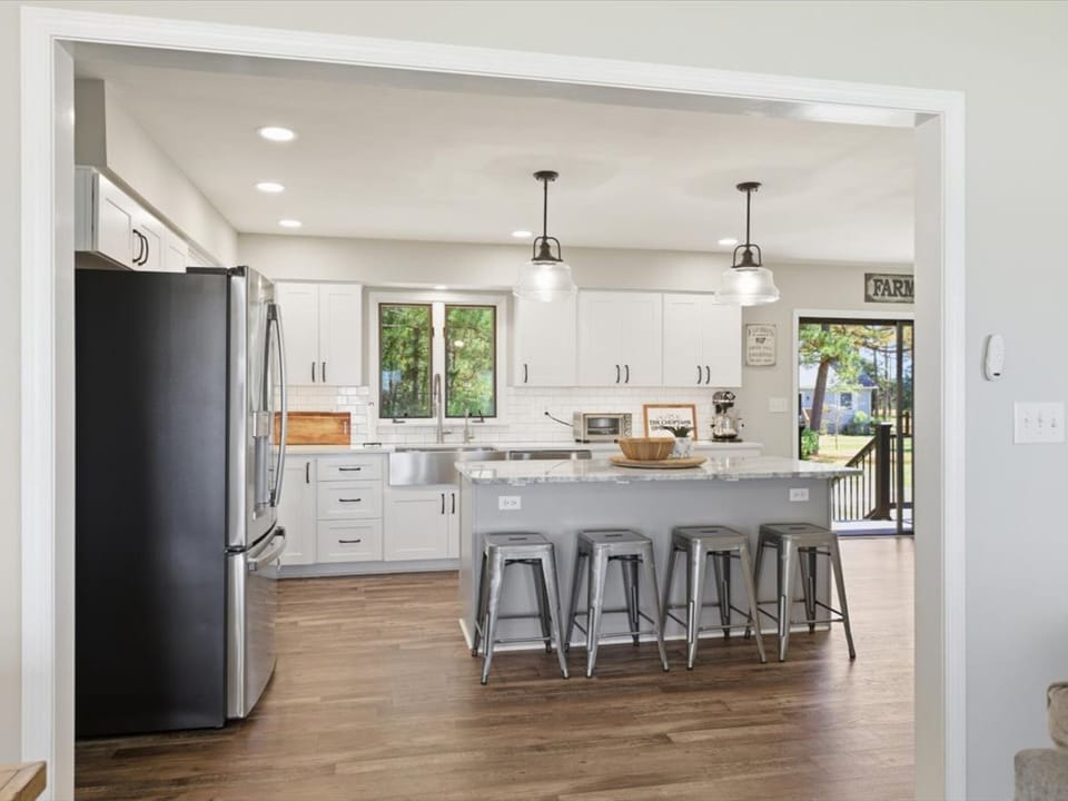 Picture yourself prepping fresh meals in this bright, modern kitchen. Sleek white cabinetry, a spacious island with seating, and sunlit windows create a cheerful space where you'll gather, cook, and connect.