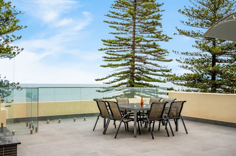 This spacious outdoor terrace features a sleek dining set with seating for eight, set against a backdrop of pine trees and ocean views—perfect for alfresco meals or sunset gatherings by the sea.