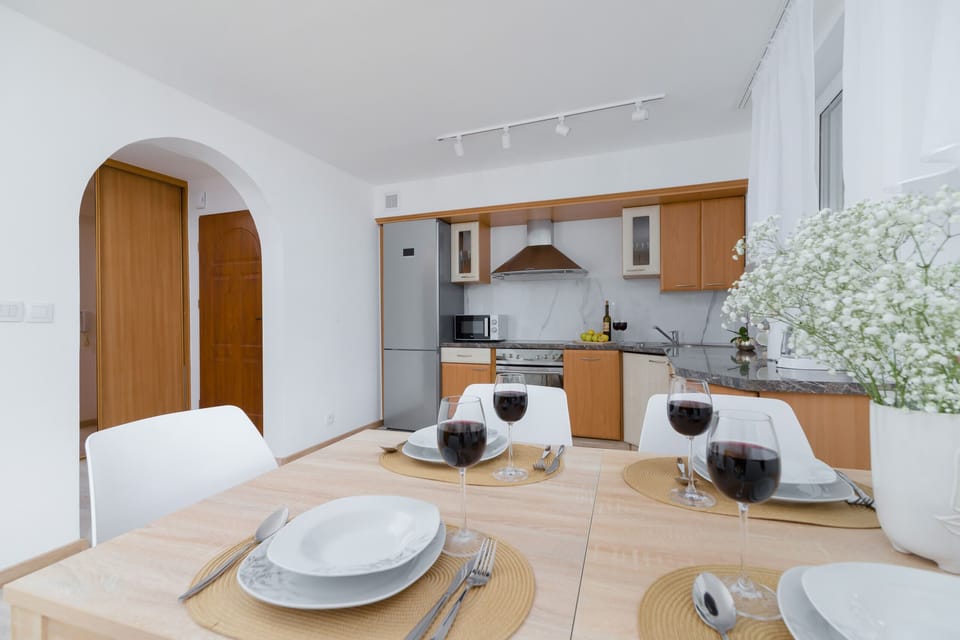 A fully equipped kitchen with light wood cabinets, white countertops, and modern appliances, connected to the dining area.