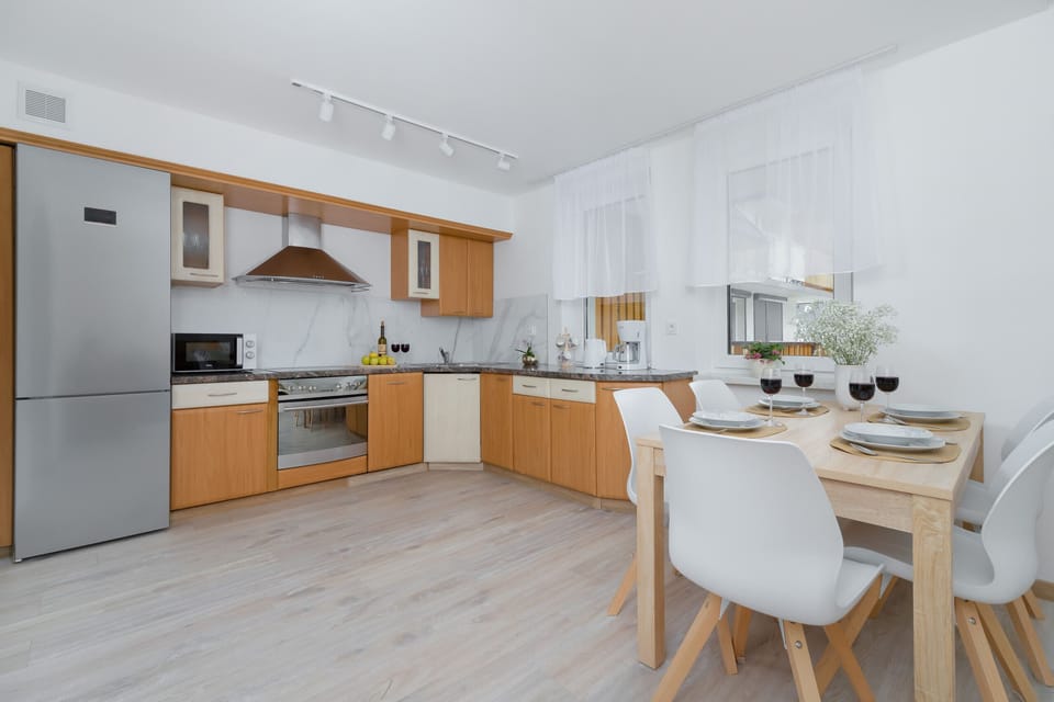A fully equipped kitchen with light wood cabinets, white countertops, and modern appliances, connected to the dining area.