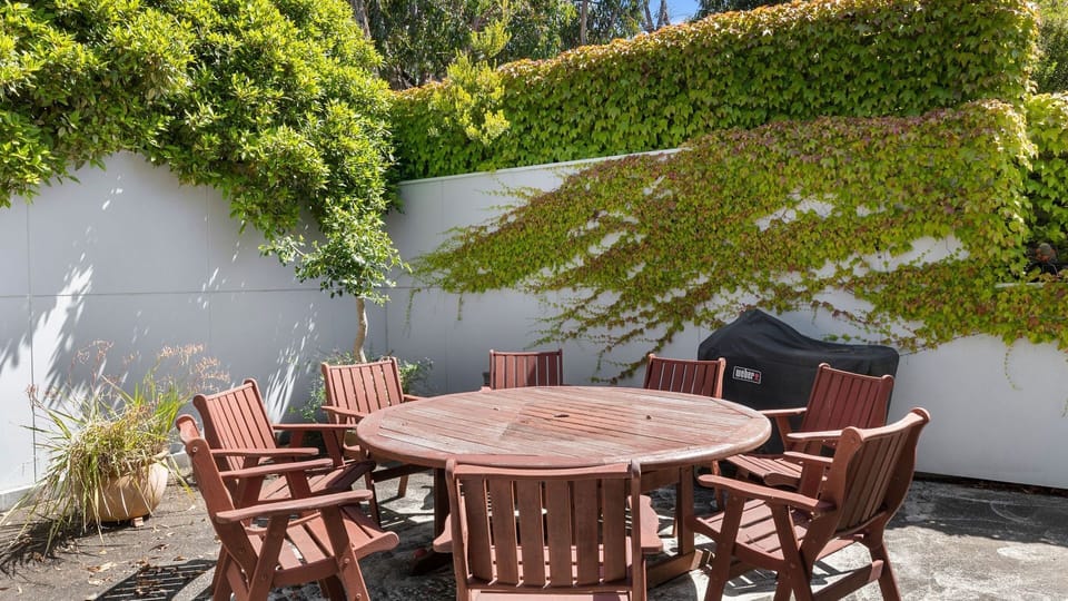 It features a lovely courtyard with an outdoor dining set that faces a well-kept lawn and a garden with impressive shrubbery.