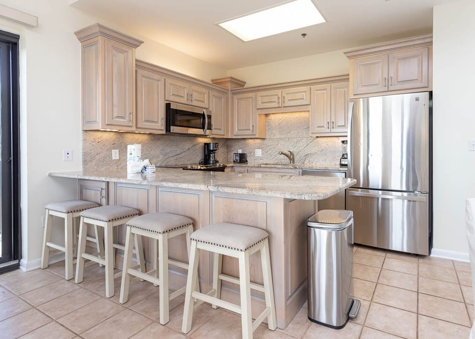 Light wood cabinetry and granite countertops enhance this modern kitchen with a breakfast bar and four stylish stools