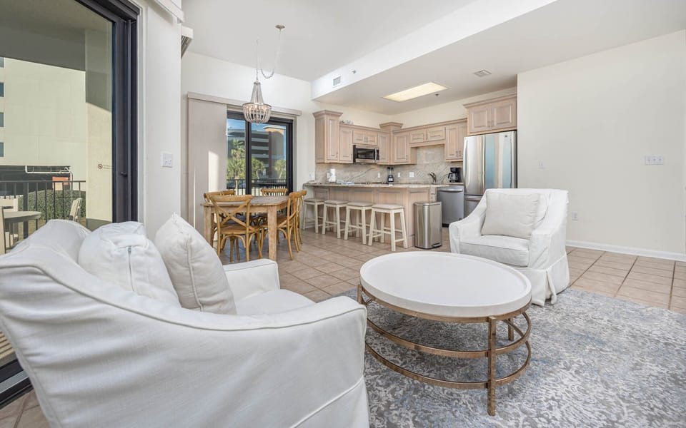 Living area featuring white seating, a round coffee table, and a dining space adjacent to a kitchen with light cabinetry