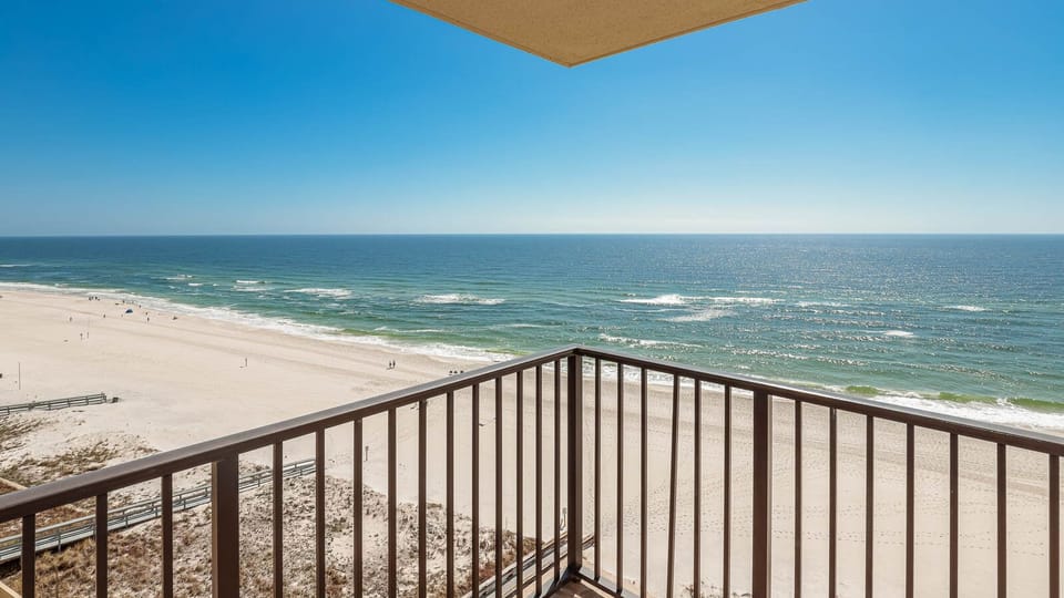 The balcony offers a panoramic view of the sparkling water and white sand beach, inviting relaxation and enjoyment