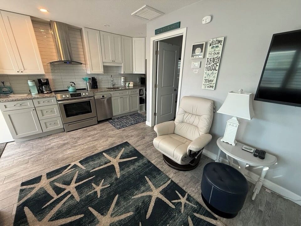 Relax in your open-concept space where modern kitchen meets cozy living area, complete with comfortable seating and beach-themed touches.