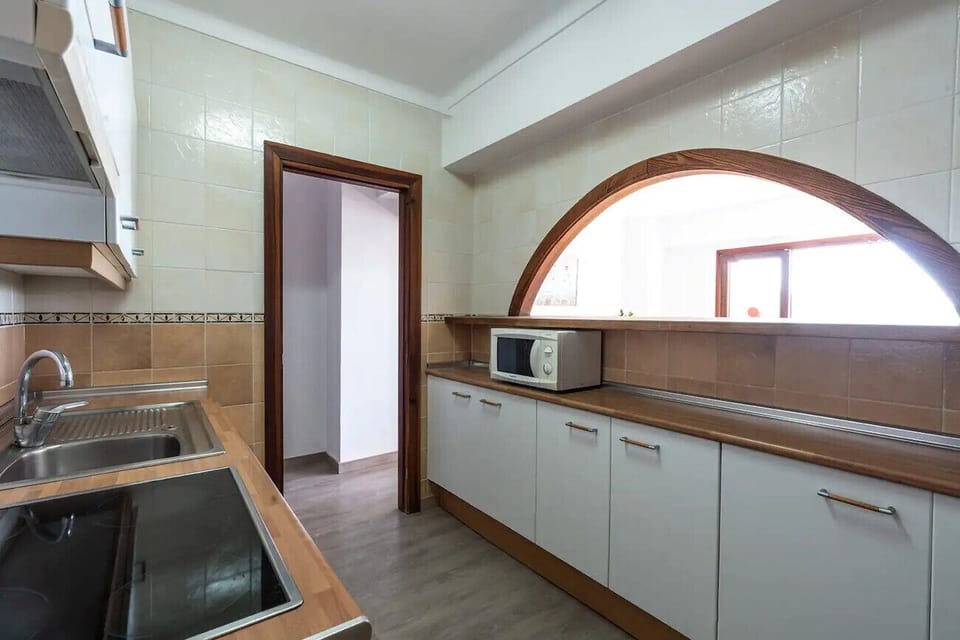 Practical kitchen with white cabinets, wooden countertop and a large arched opening connecting to the living room, bringing in natural light and a spacious feel.