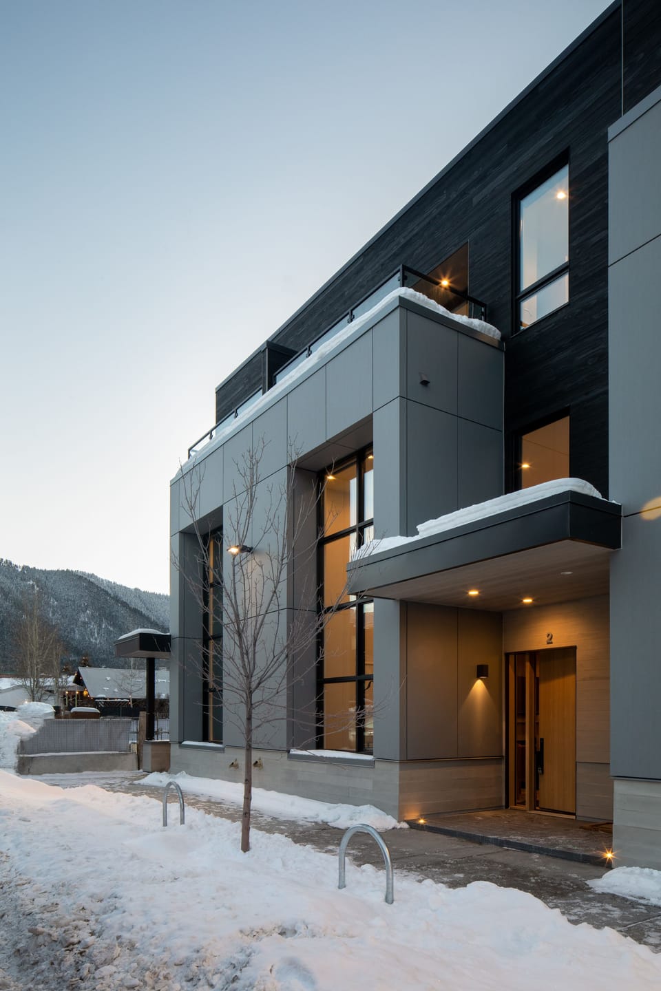 Step into your stylish mountain retreat where modern architecture meets alpine charm. The warm glow from your windows creates a welcoming beacon against the crisp winter landscape.