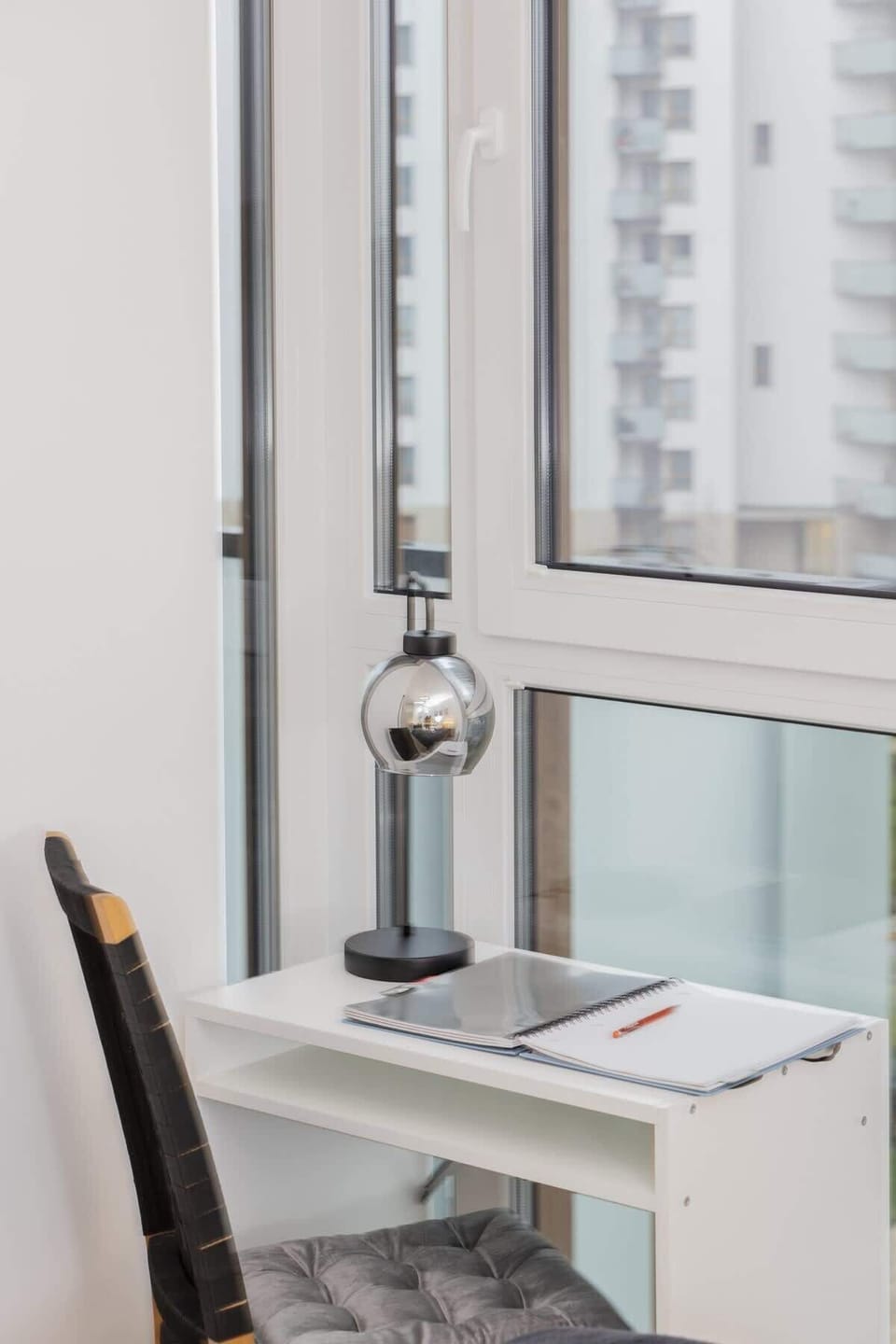 A small desk and chair are placed by a window, creating a bright and practical workspace. The window allows for plenty of natural light, making it ideal for working or studying.