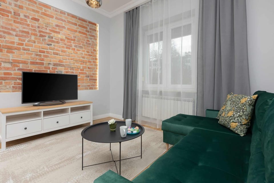 A modern living area with a brick accent wall, TV, and a plush green sofa.