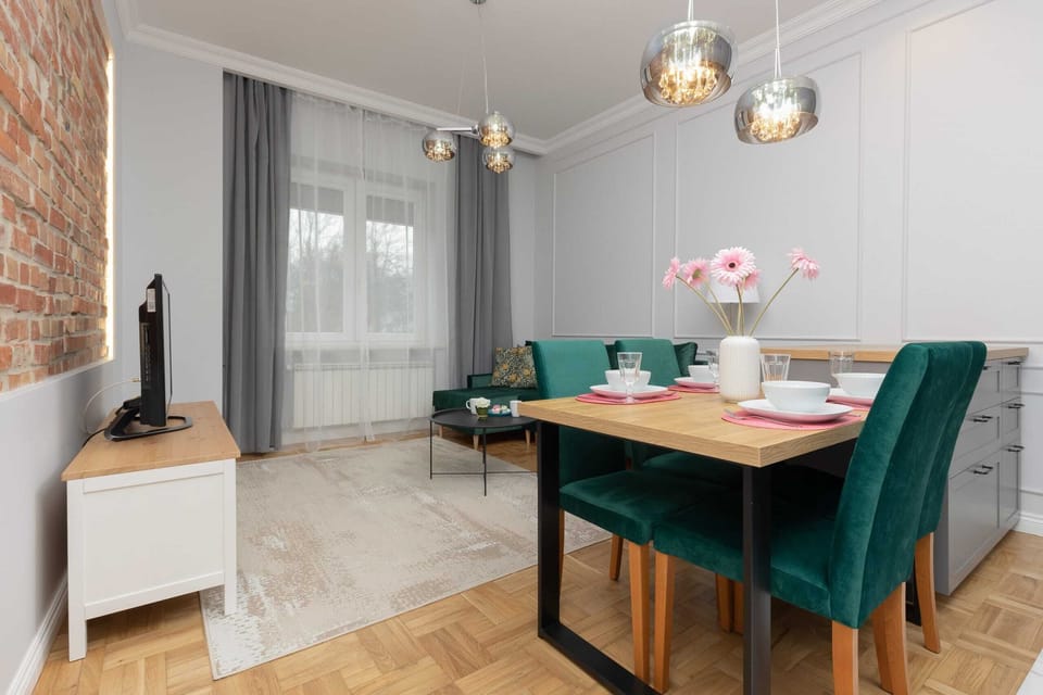 A spacious dining space with green chairs, wooden accents, and a modern kitchen in the background.