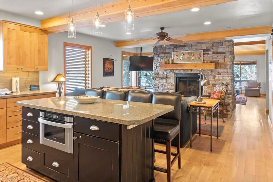 The spacious open kitchen and living room are filled with charming features such as exposed wood ceiling beams, a beautiful stone hearth double-sided fireplace, and modern light fixtures.