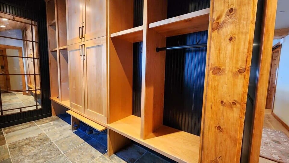 The large mudroom features built-in cabinet and shelving space, a long bench to sit on, and several coat hooks.