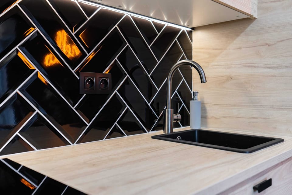 A stylish kitchen with wooden cabinetry, black backsplash tiles, and modern appliances.