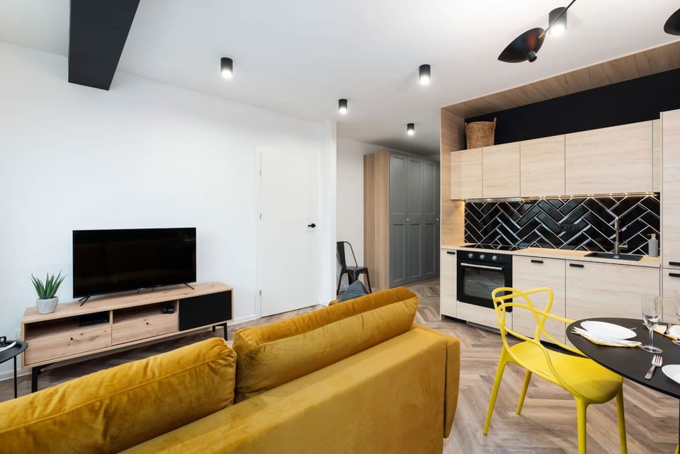 A modern kitchen featuring a herringbone black tile backsplash, light wood cabinets, and a stove.