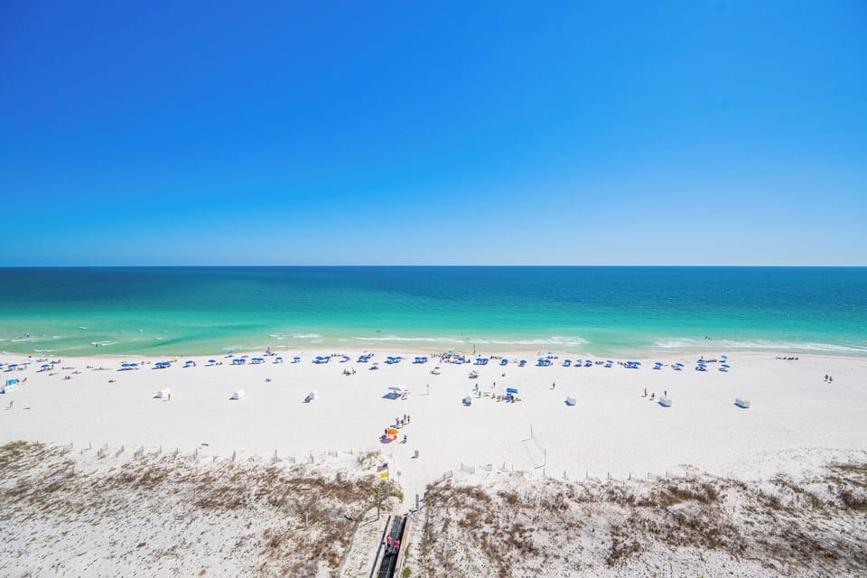 Endless blue stretches above the turquoise coast where colorful umbrellas dot the shore below