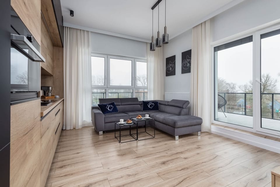 A bright living room with large windows, gray sofas, and a sleek TV area.