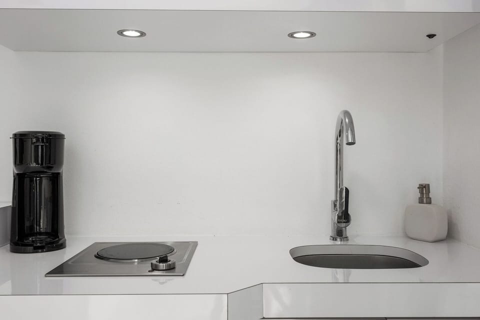 An electric stove top with 1 burner, sink, coffee maker.
