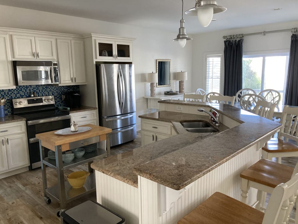 Open view of kitchen, bar with 6 chairs, and dining area
