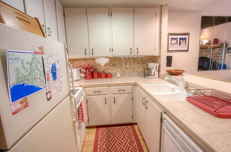 Kitchen with refrigerator, range, counter, sink, dishwasher, map on refrigerator, and living room visible in mirror.