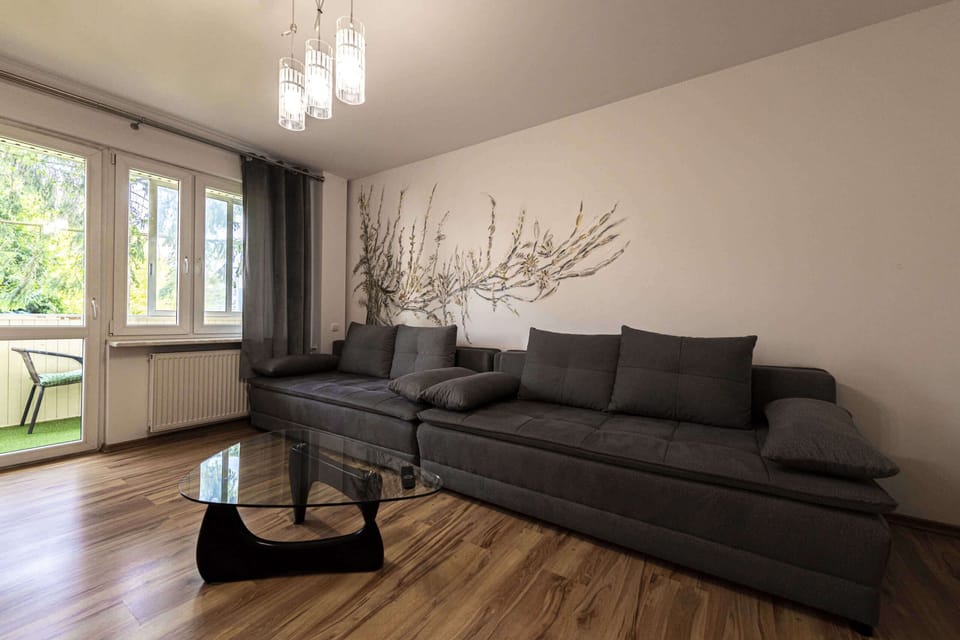 A cozy living room with a grey sofa, decorative wall art, and wooden flooring.
