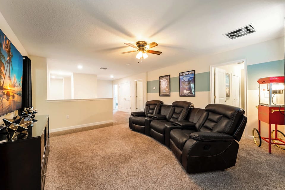 Private movie lounge with reclining leather theater seats, framed film posters, a large-screen TV, and a classic red popcorn cart.