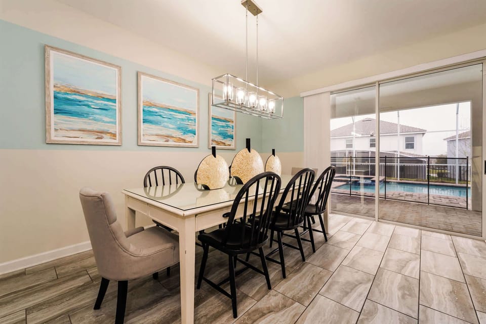 Private dining room with seating for a large group, coastal artwork, a glass chandelier, and sliding doors opening to the screened pool deck.