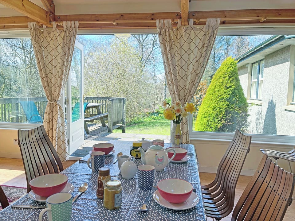 Breakfast table with doors out to decking and steps down to garden. Bedroom wing on right | Garrique Cottage, By Kippen, near Stirling