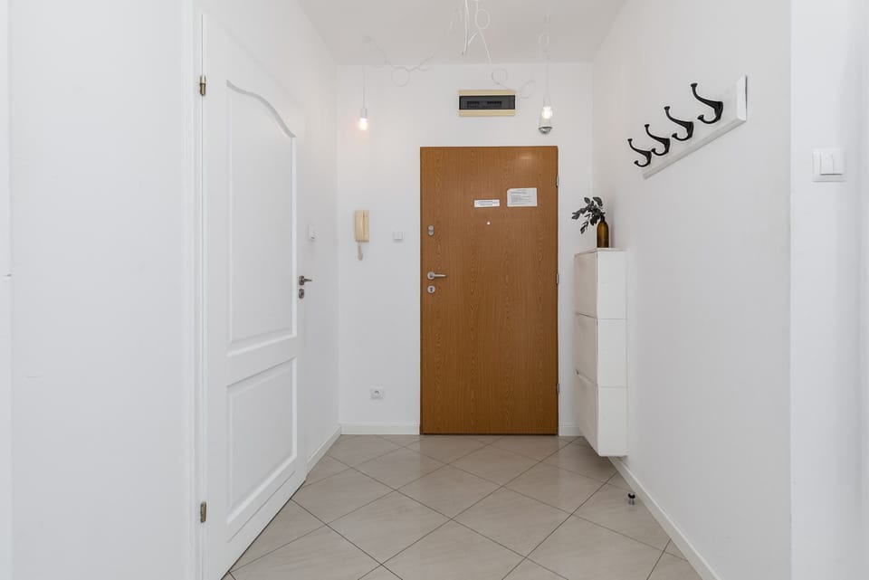An entryway with a wooden door, white walls, and wall hooks.
