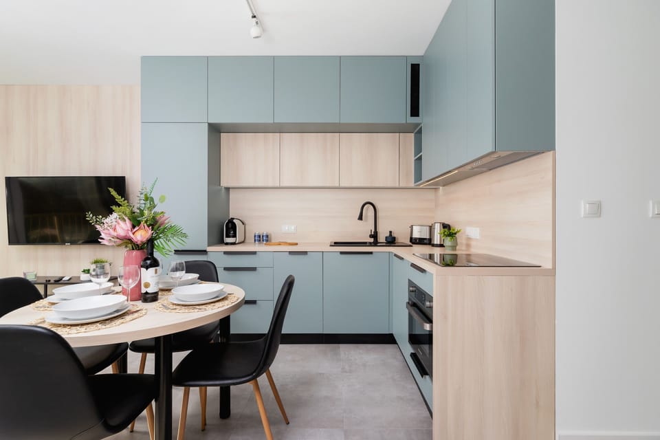A modern kitchenette with pastel cabinets, a wooden countertop, and decorative flowers.

