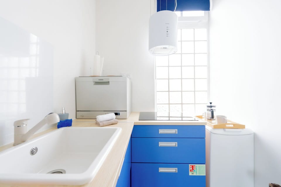 Bright kitchenette with blue cabinets, cooktop, and countertop dishwasher.