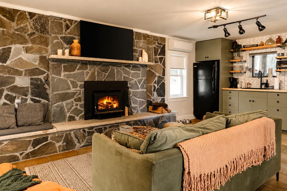 Movie nights are easy on the green sofa with the TV mounted above the stone fireplace; the wood-burning fire adds warmth on chilly Upstate New York evenings.